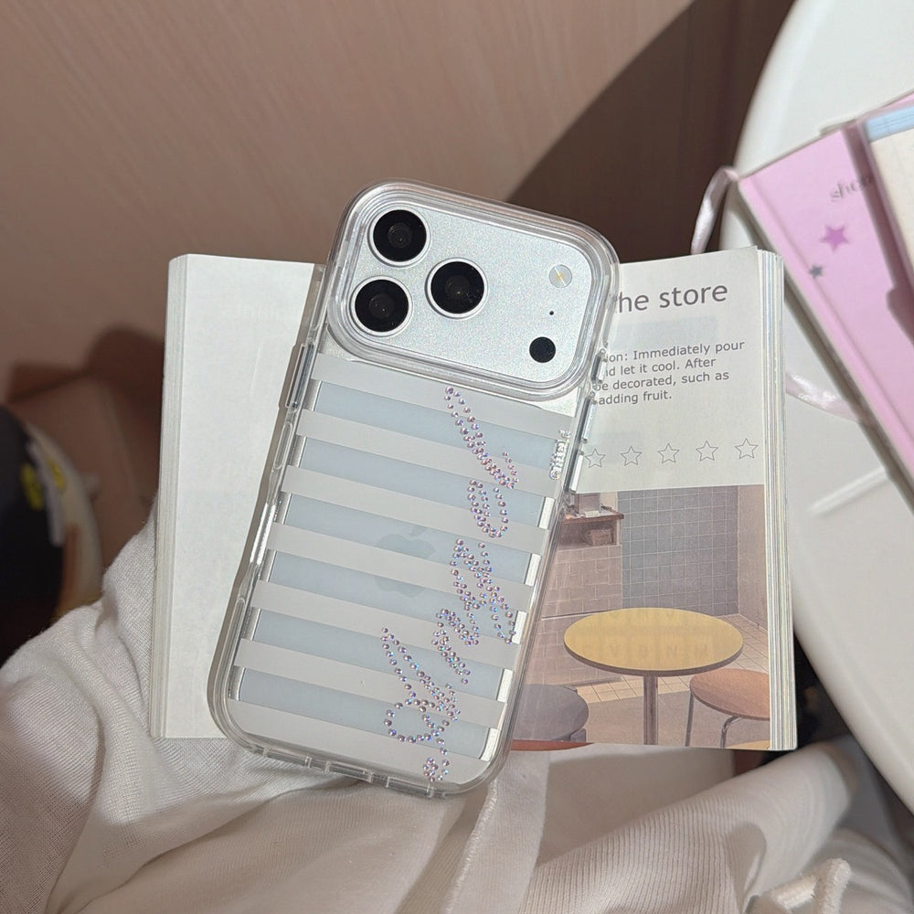 A silver-framed striped iPhone case with a purple rhinestone crystal Angel layout resting vertically on an open store magazine.