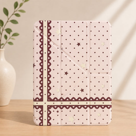 Kawaii coquette pink lace ribbon iPad smart case standing vertically on a wooden table next to a white ceramic vase with green leaves.