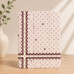 Kawaii coquette pink lace ribbon iPad smart case standing vertically on a wooden table next to a white ceramic vase with green leaves.