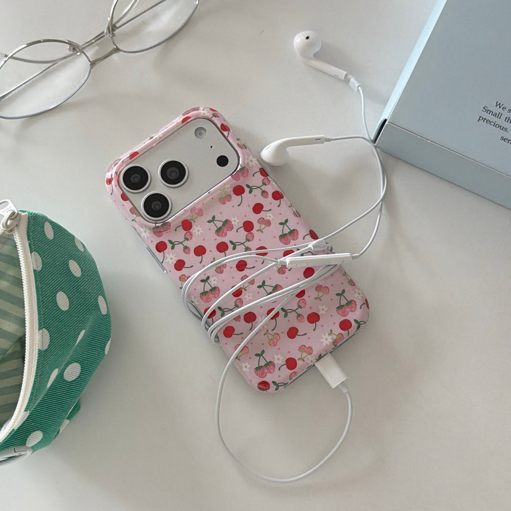 A coquette pink cherry phone case wrapped in white wired earphones next to a green polka dot pouch.