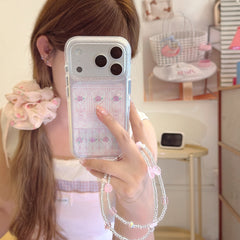 A mirror selfie showing a silver iPhone case with a pink rose gate pattern and a beaded wrist strap.