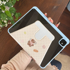 Overhead view of a handheld iPad with a soft girl aesthetic light blue case, showcasing the clear acrylic back pane and the geometric lines of the beige magnetic folding stand.