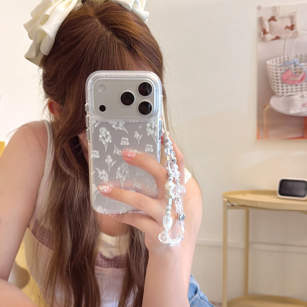 A mirror selfie of a girl with a white hair bow holding a clear iPhone case with a white iris floral sketch.