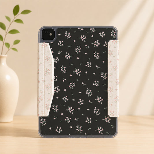 Front-facing studio shot of a cottagecore floral iPad case standing on a wooden desk next to a white vase with green leaves.