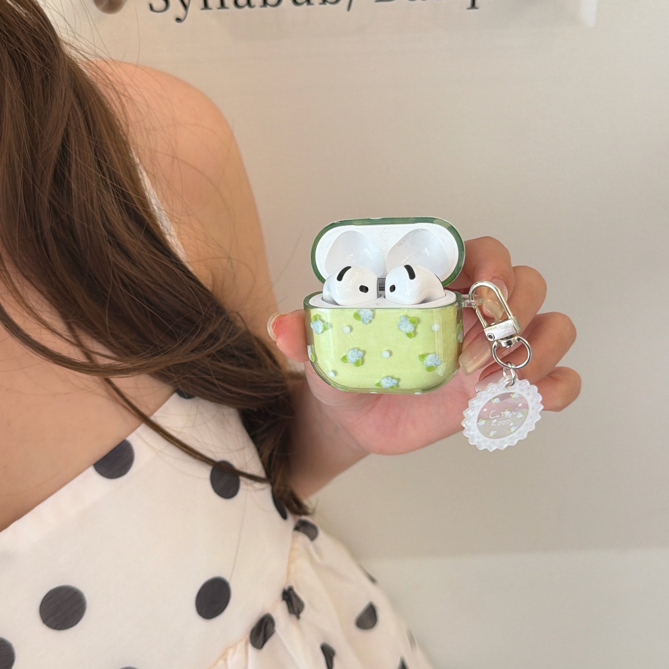 A girl in a polka dot dress holding an open matcha green floral AirPods case with white earbuds.