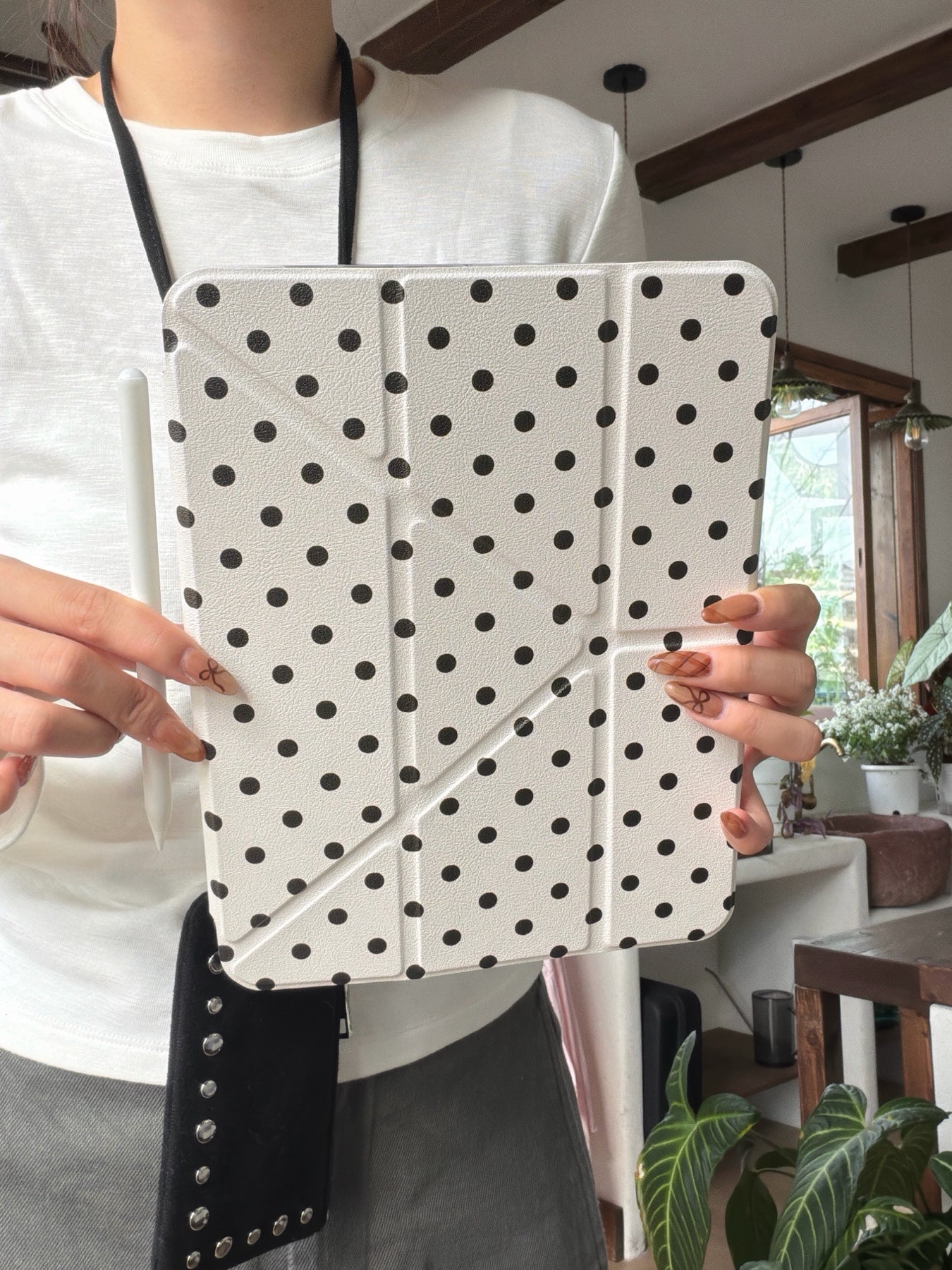 A mid-section view of a person holding an ivory cute aesthetic ipad protective shell vertically while resting a white stylus pen on the left side.