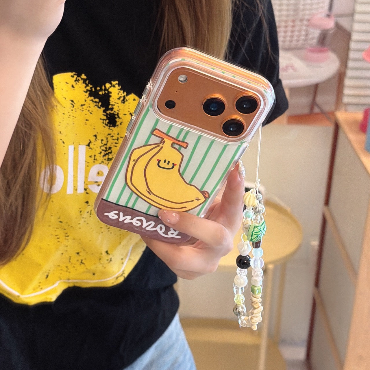 Close-up of a bronze iPhone protected by a green striped phone cover with a funny smiling banana cartoon design.