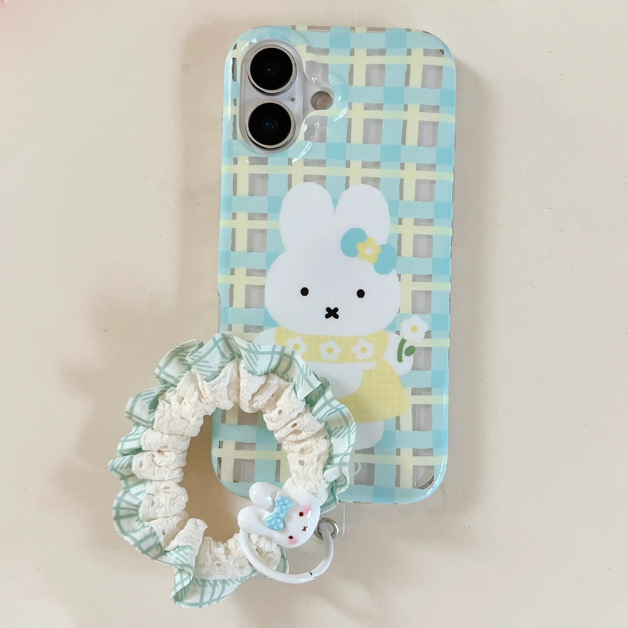 A pastel blue and yellow gingham plaid phone case featuring a white cartoon bunny with a green lace scrunchie strap.