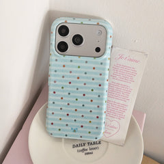 A cute blue polka dot phone case standing on a white ceramic plate next to a romantic French text card.