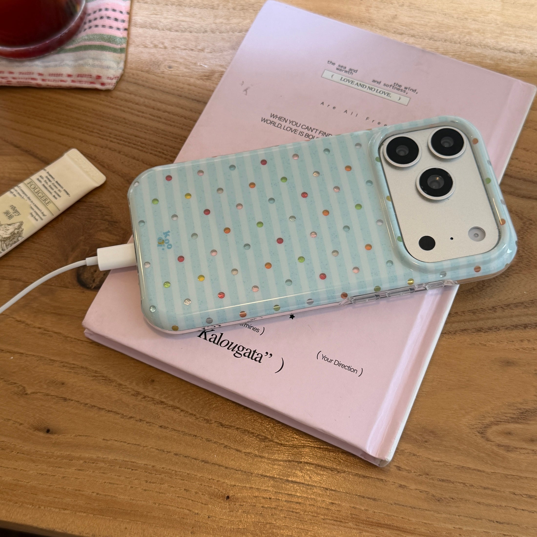 A cute blue striped phone case connected to a charging cable while resting on a pink book.