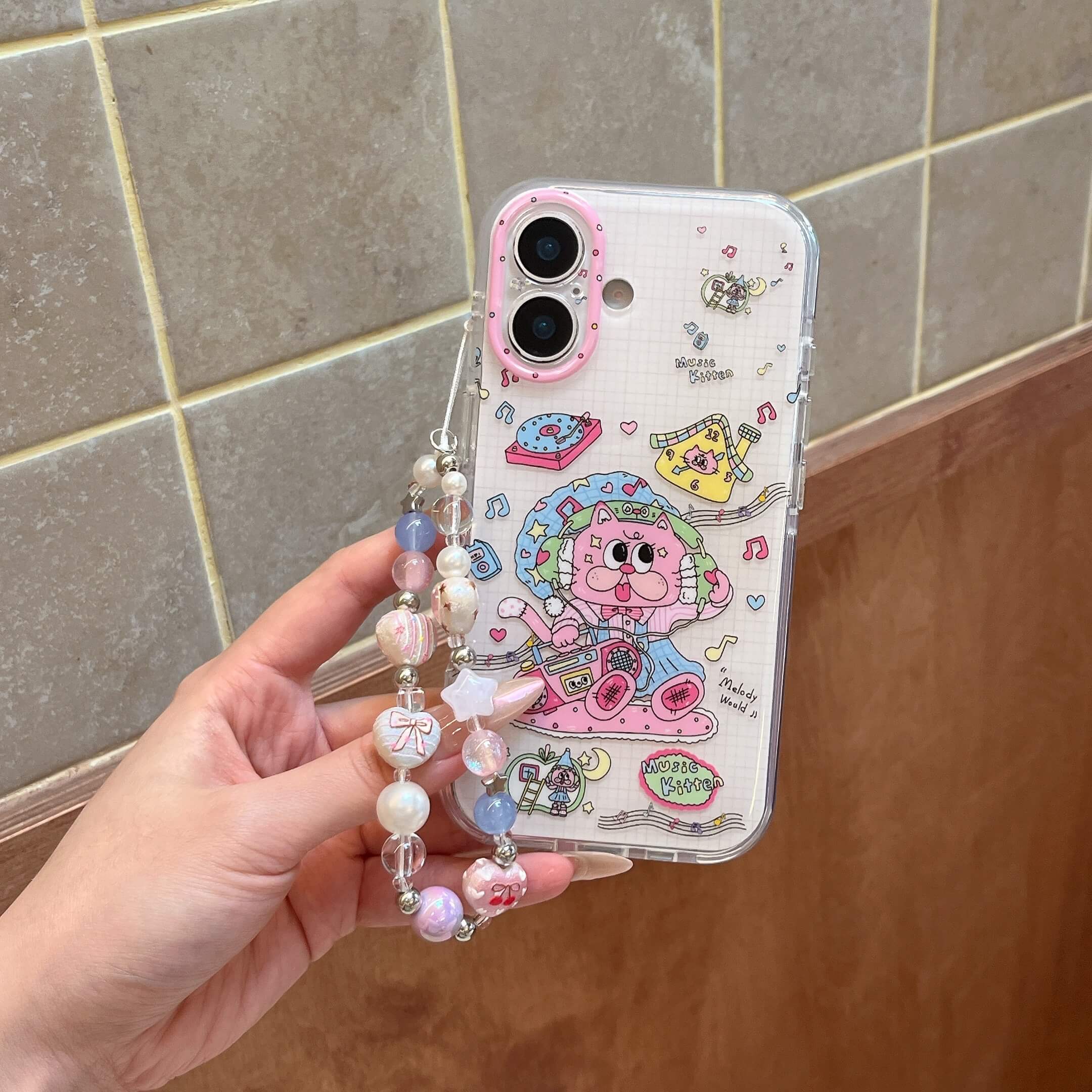 Hand holding a cute cartoon cat phone case with a hanging pastel beaded wrist strap.