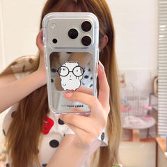 Mirror selfie showing a girl holding a cute cartoon hamster mirror iPhone case with a silver camera frame.