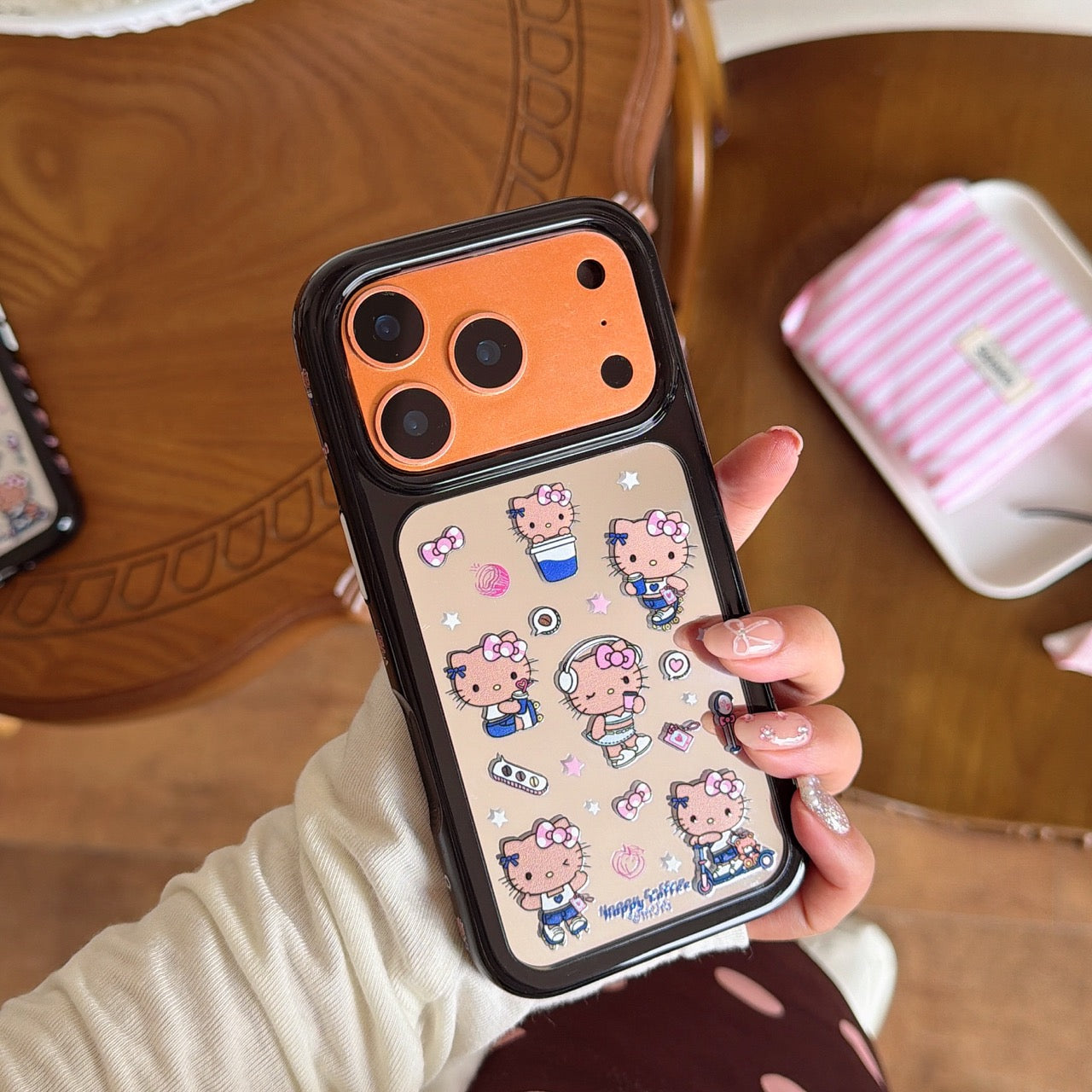 Hand holding a cute cartoon Hello Kitty mirror phone cover featuring a matte orange camera lens protection module.