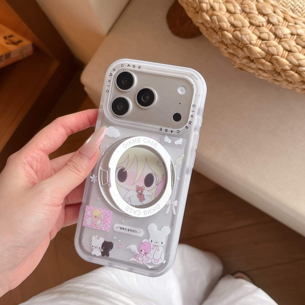 A hand showcasing the back of a cute cartoon girl iPhone case with an integrated silver ring stand.