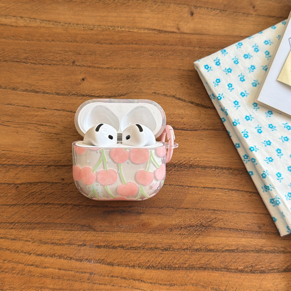 An open cute cherry AirPods case standing upright on a wooden desk next to a blue floral cloth.