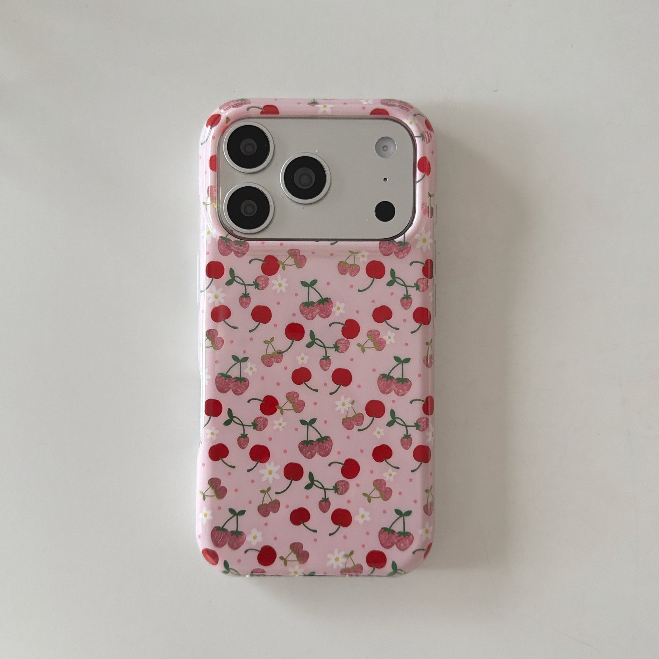 Flat lay back view of a cute cherry pink iPhone case with floral patterns on a white surface.