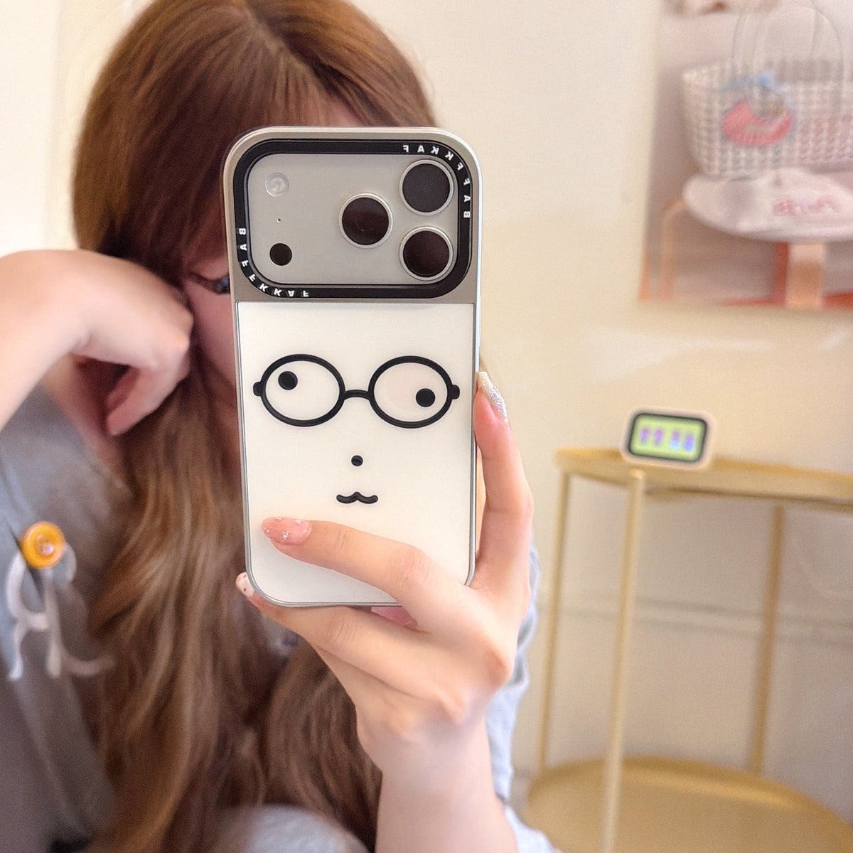 Mirror selfie showing a cute geek face phone cover with a silver camera frame.