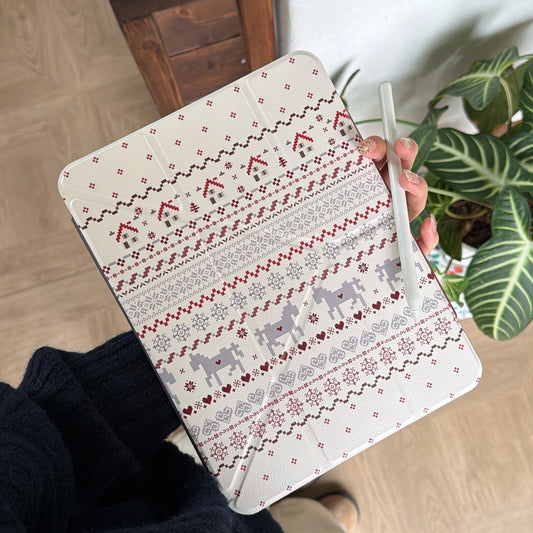 A handheld shot of a cute geometric winter iPad shell featuring red and grey knitwear patterns against a background of green houseplants.