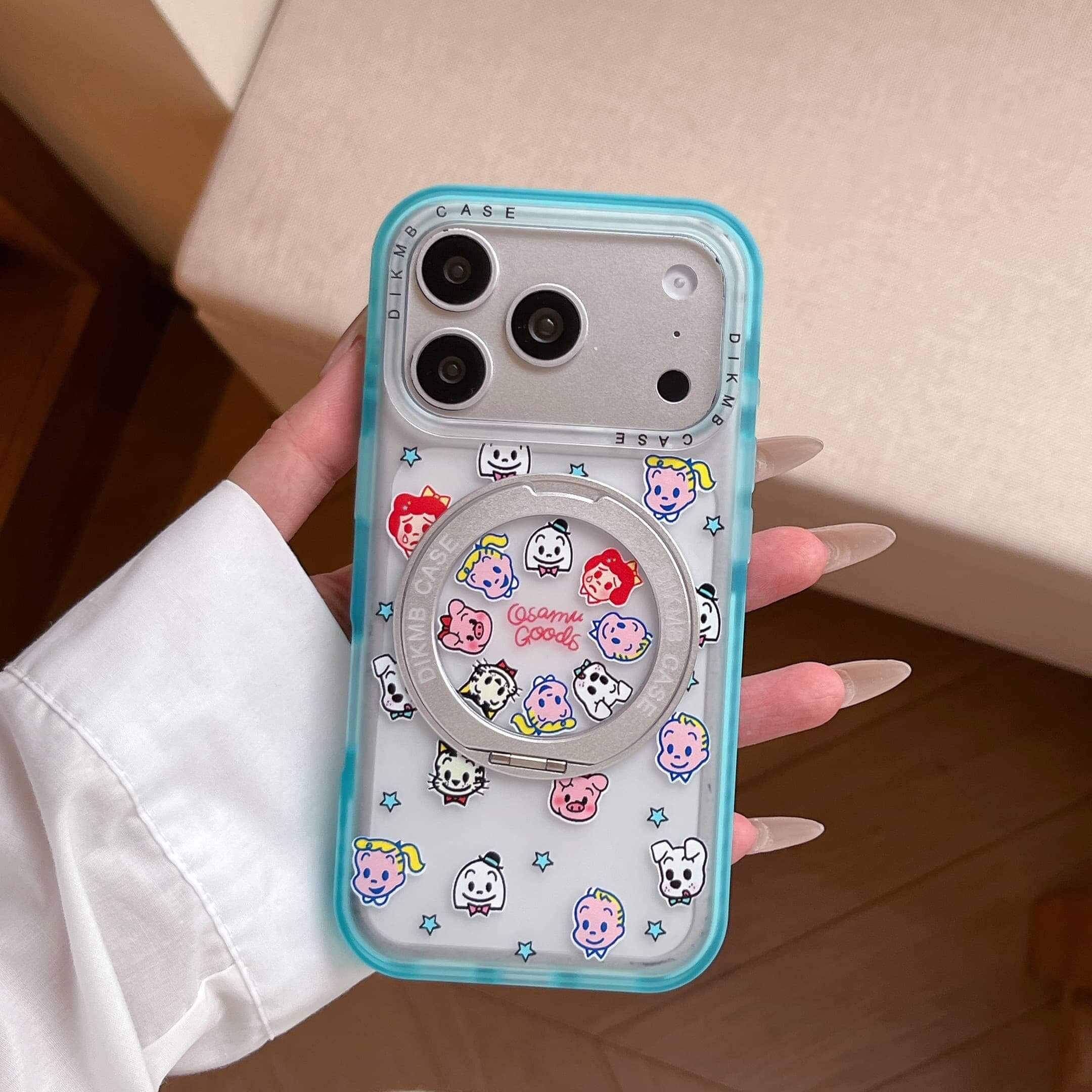 A hand holding a cute Japanese cartoon phone case with a translucent blue edge on a coffee table.