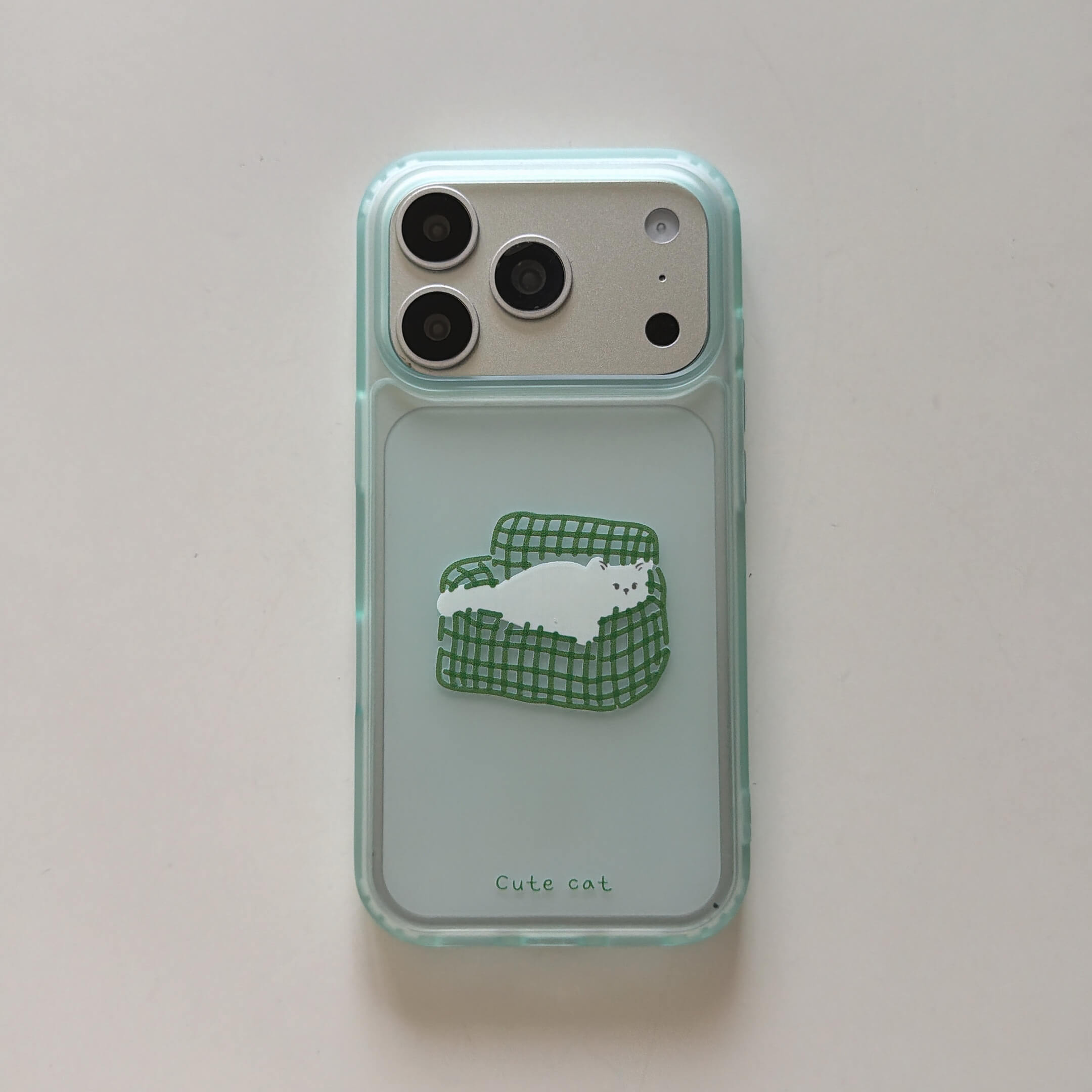 A flat lay view of a clear aesthetic iPhone case featuring a cute cartoon white cat on a green sofa on a white background.