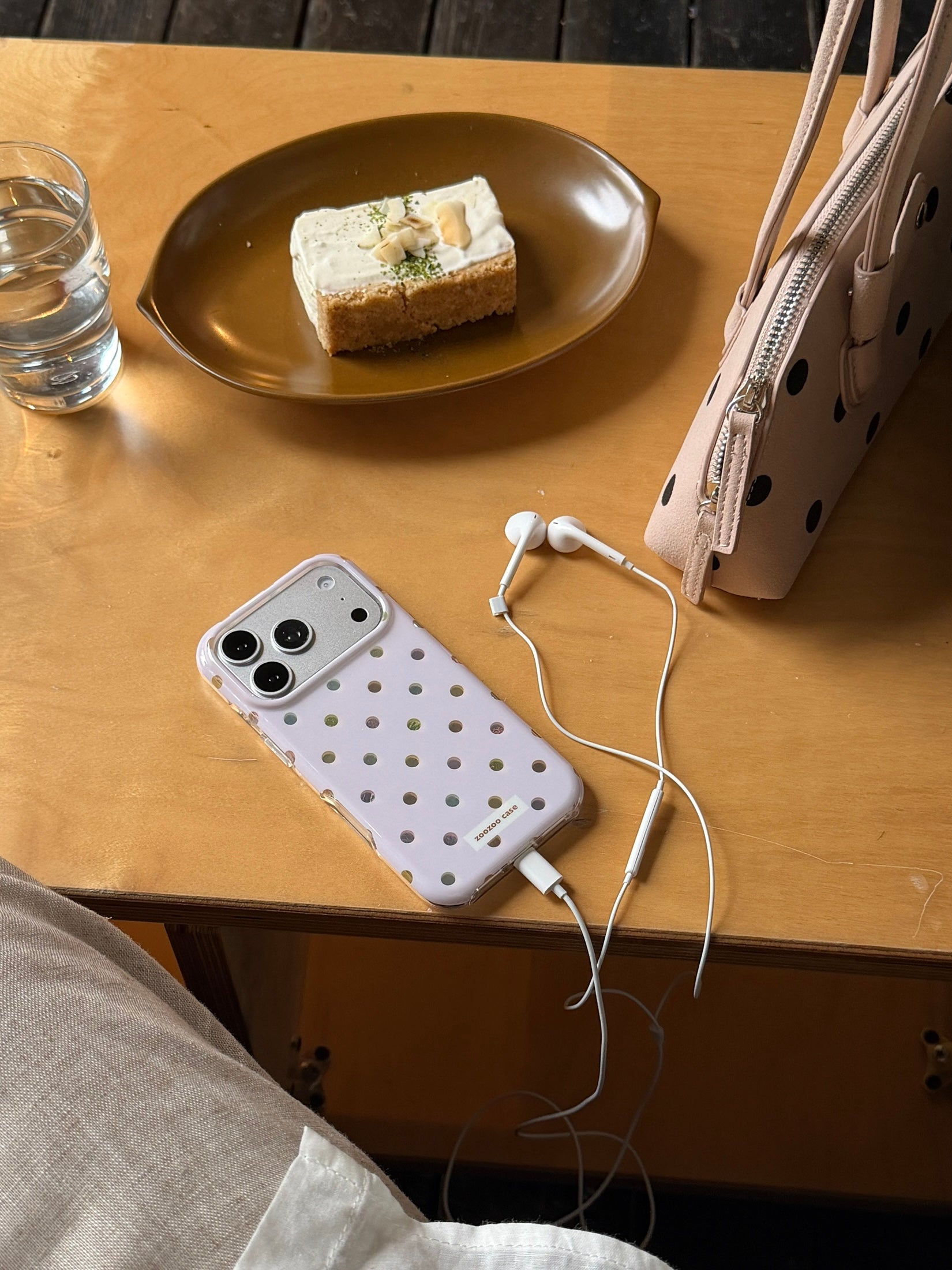A cute lavender polka dot iPhone case with white earphones plugged in on a wooden desk.