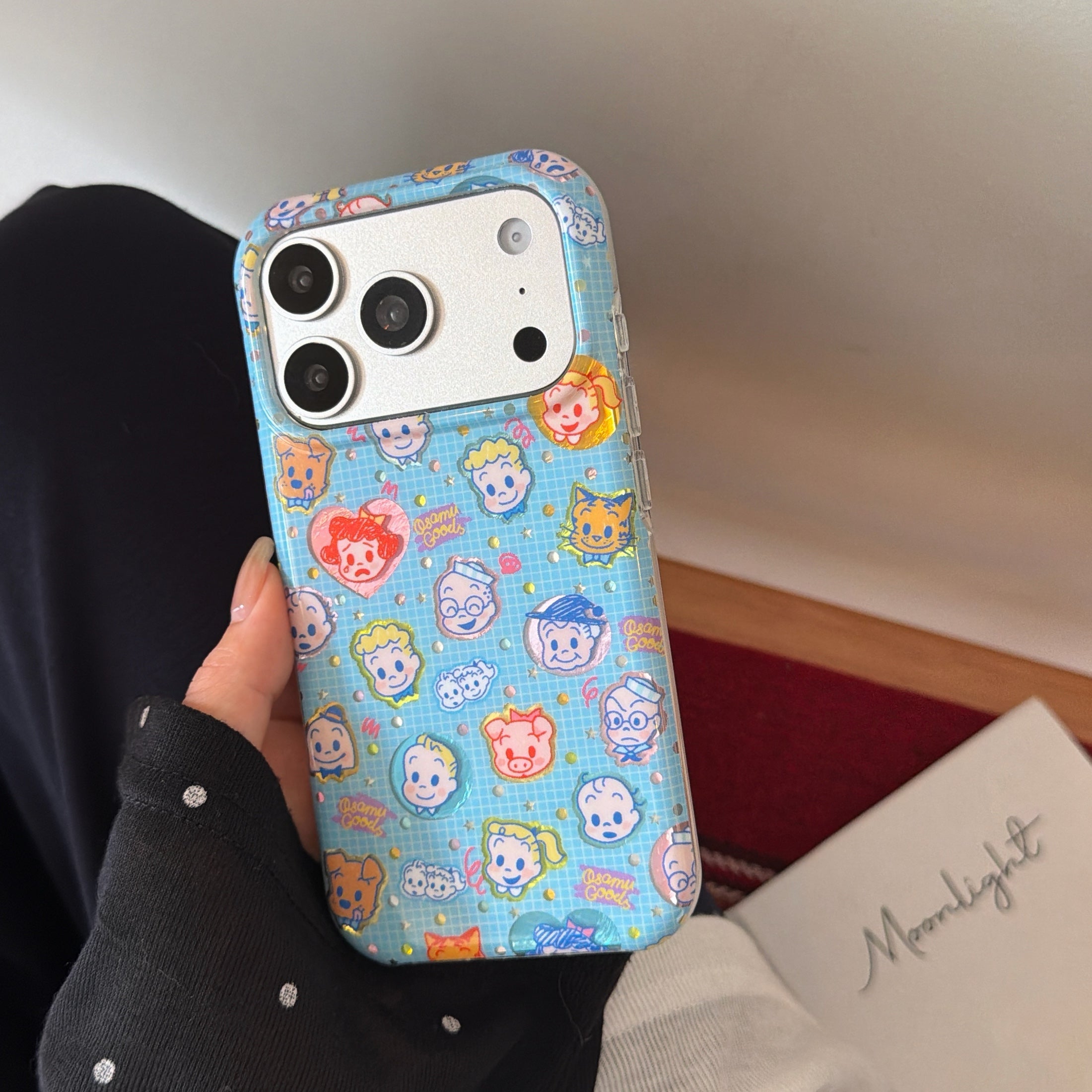 Hand holding a cute Osamu Goods phone case next to a white notebook displaying the word Moonlight.