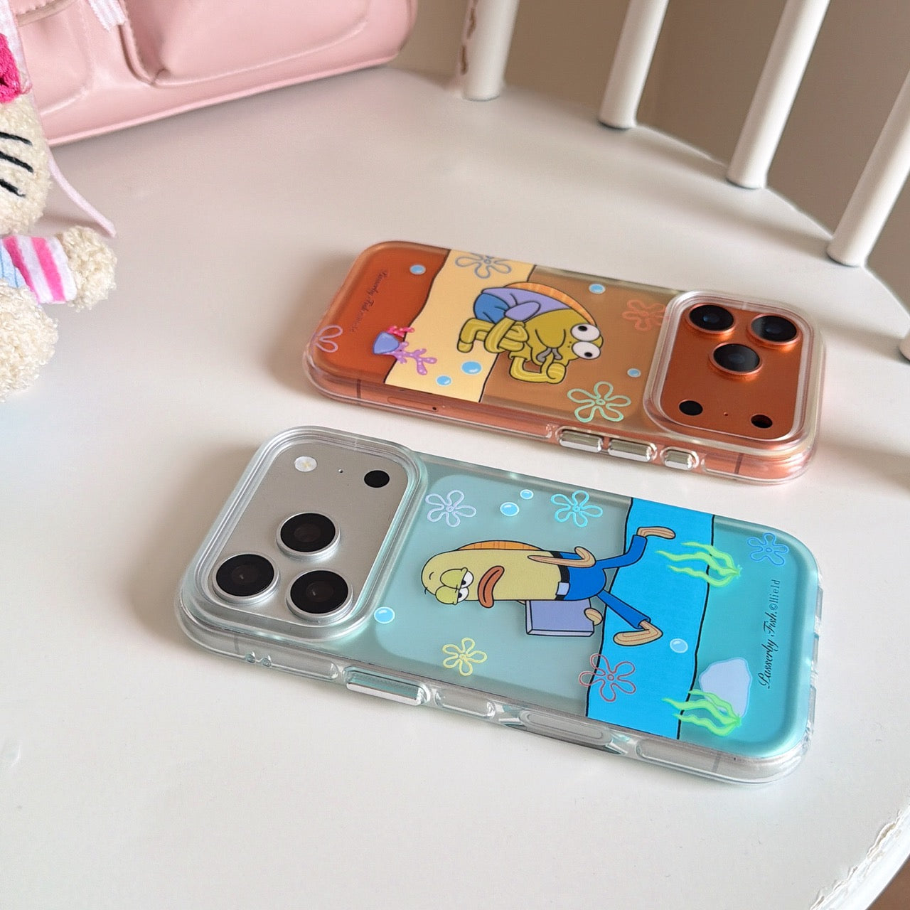 An orange and a light blue clear phone cover with funny animated fish graphics resting on a white chair.