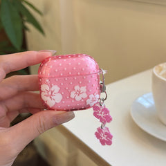 A hand holding a translucent pink hibiscus flower AirPods Pro case with a double flower charm keychain.