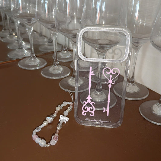 A cute clear phone case with pink keys standing in front of rows of reflective wine glasses.