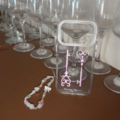 A cute clear phone case with pink keys standing in front of rows of reflective wine glasses.