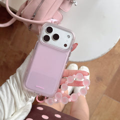 High-angle shot of a hand holding a cute pink pastel phone case and pink beaded strap near a matching leather handbag.