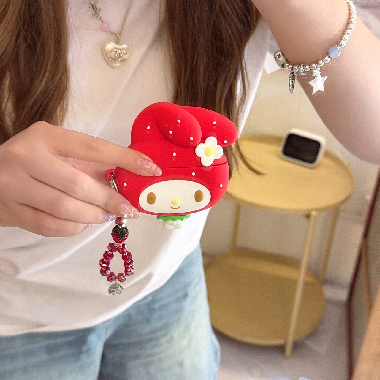 Close-up of a girl showing a red My Melody strawberry shaped AirPods Pro protective cover with a flower detail.