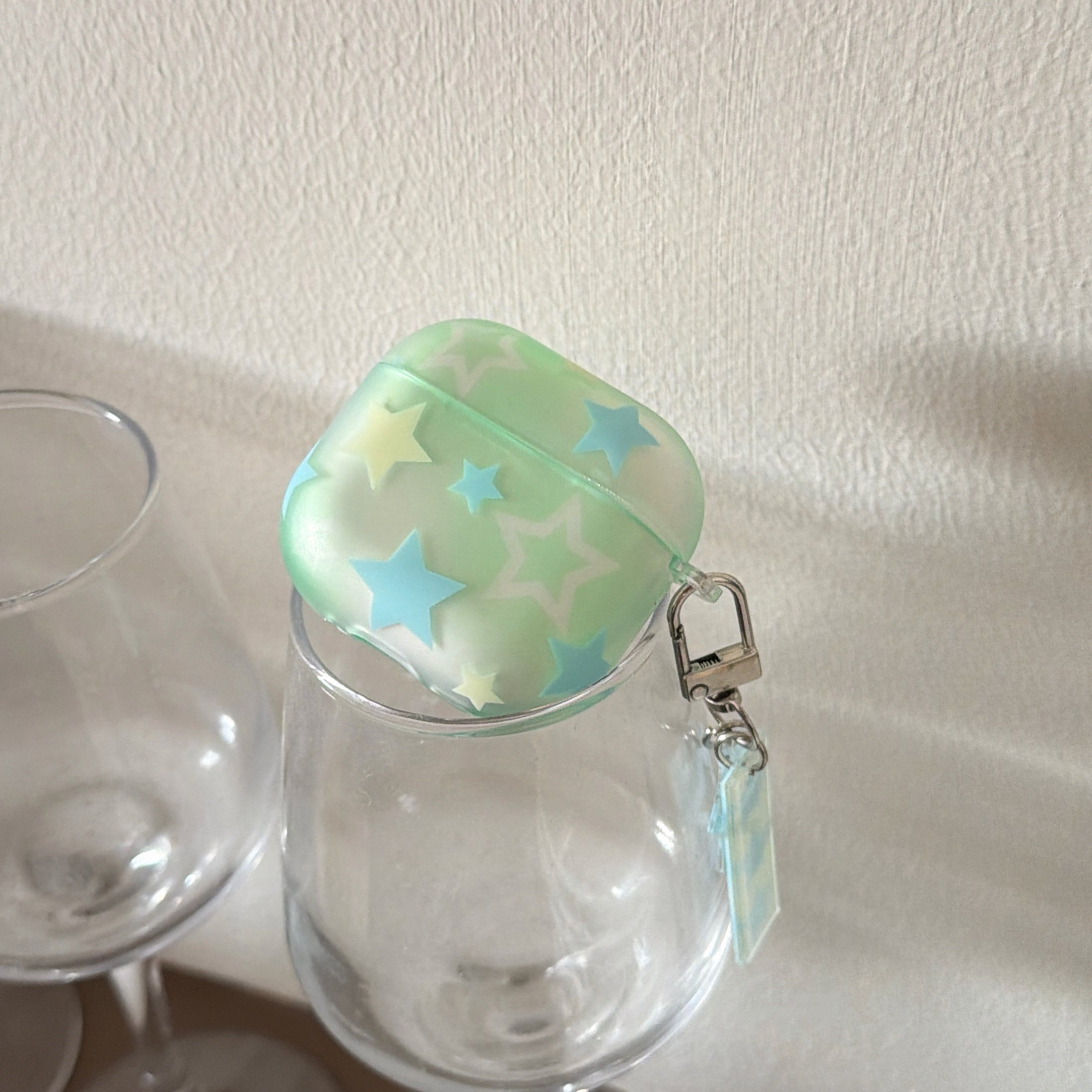 A translucent starry mint green AirPods case balanced on top of an empty clear wine glass.