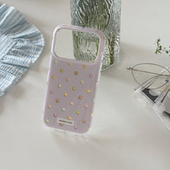 An empty purple polka dot iPhone case shell standing on a white surface next to a glass vase.