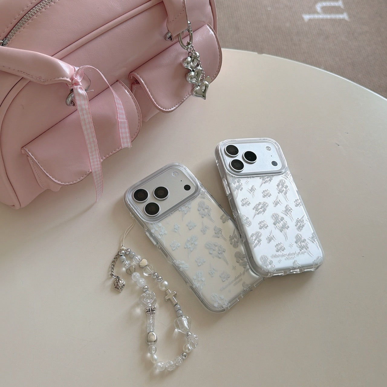 Two clear iris sketch phone cases displayed next to a pastel pink coquette aesthetic duffle bag.