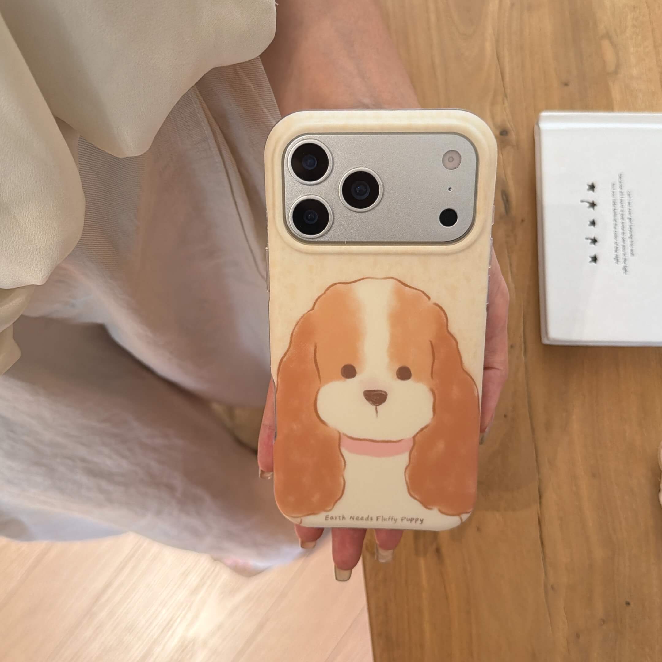 Top view of a fluffy puppy iPhone case held over a wooden floor.