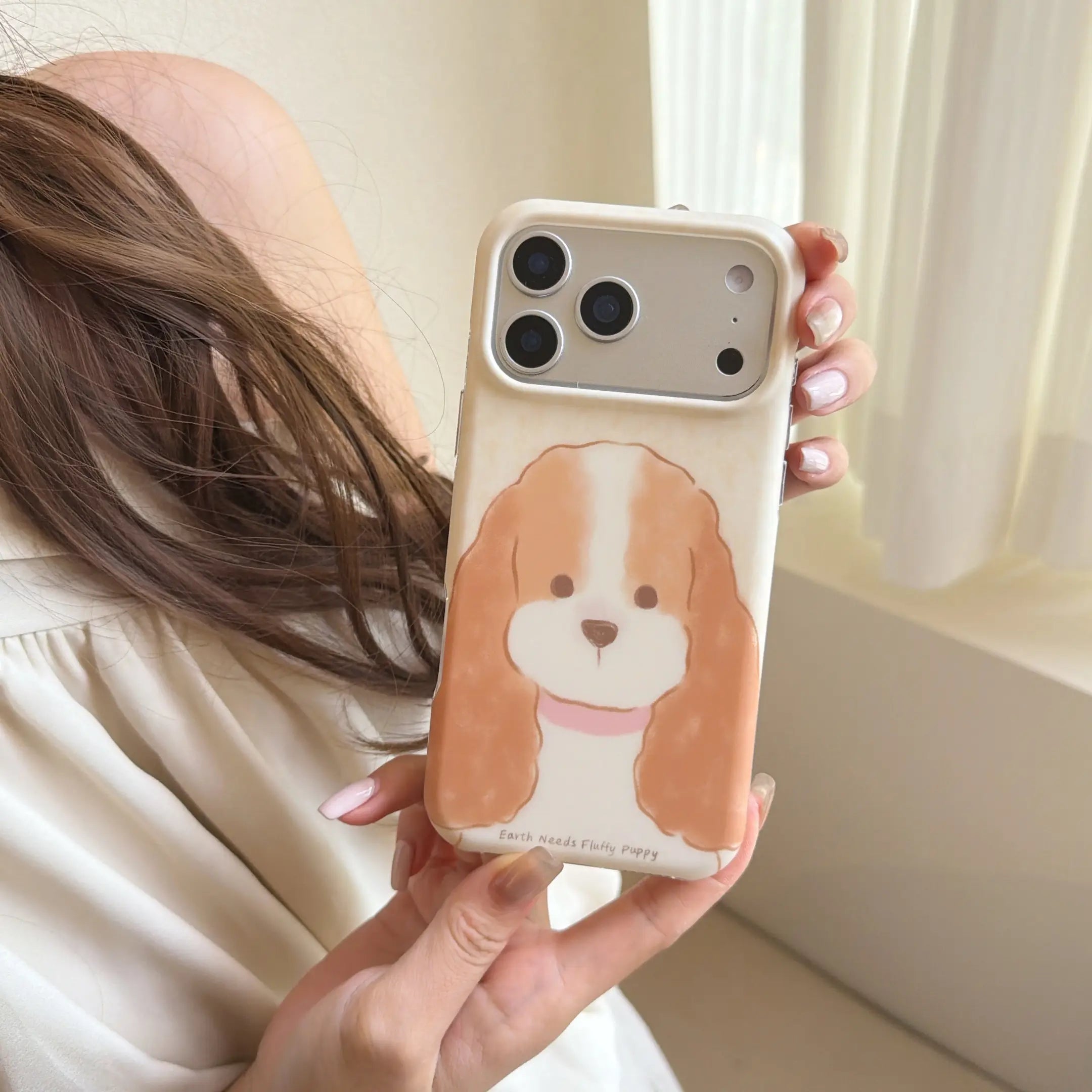 Hand holding a cream iPhone case with a fluffy long-eared puppy portrait.