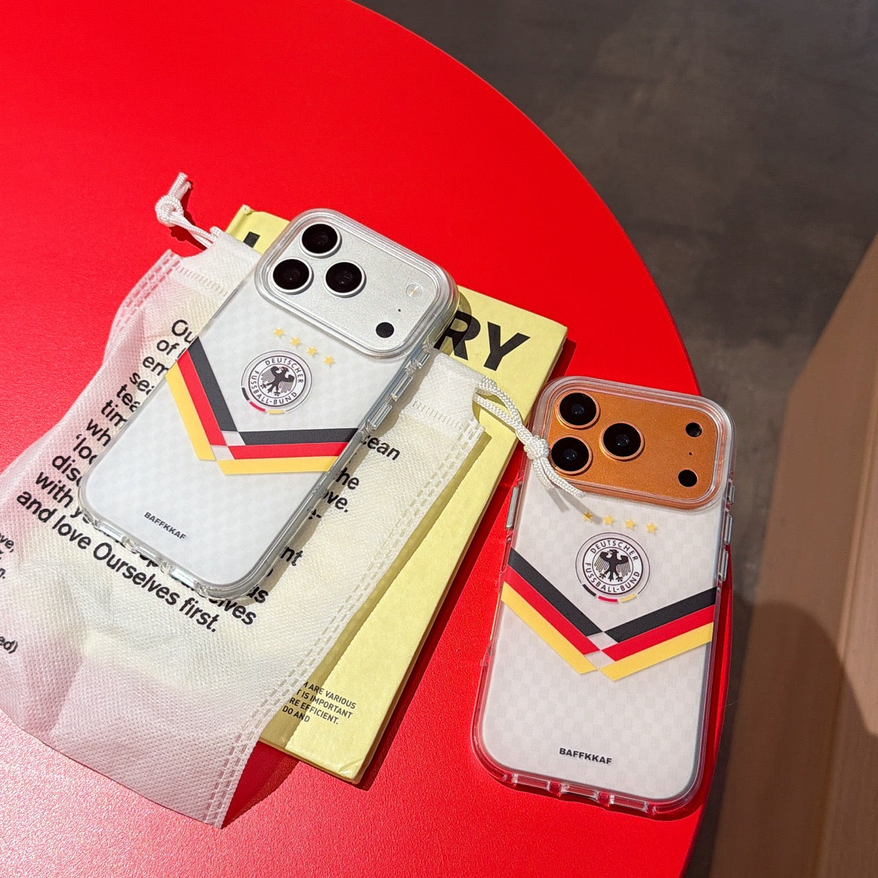 Silver and orange gold Germany mirror phone cases displayed with aesthetic lifestyle packaging on a red table.