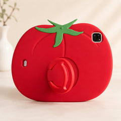Clean studio display of a funny food design ipad cover shaped like a giant red tomato, standing upright on a minimalist white surface with a blurred white decorative vase in the background.