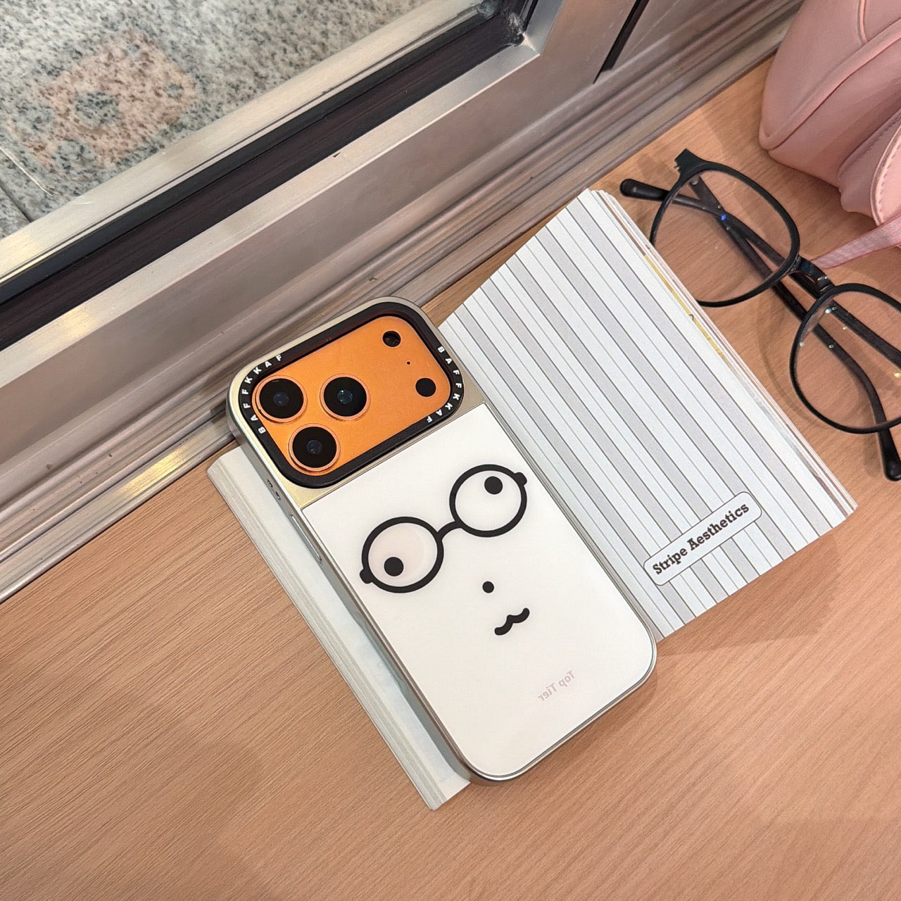 An orange-framed funny glasses iPhone case resting on an open stripe aesthetics notebook.