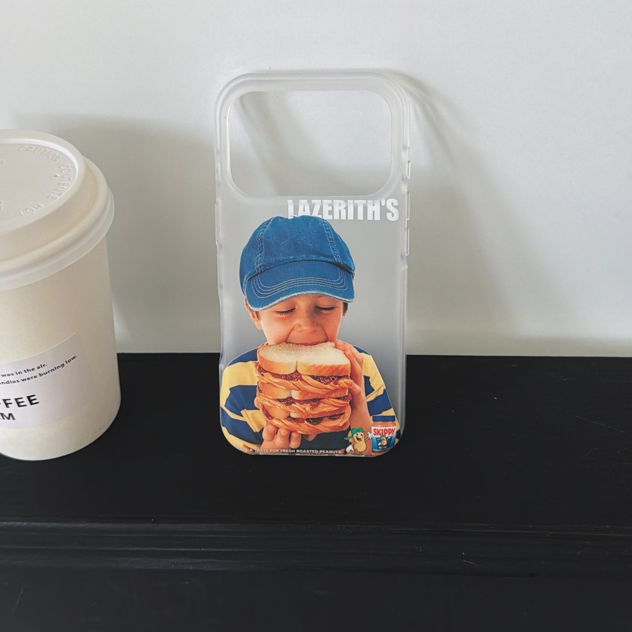 An empty funny retro sandwich boy iPhone case standing on a black shelf next to a coffee cup.