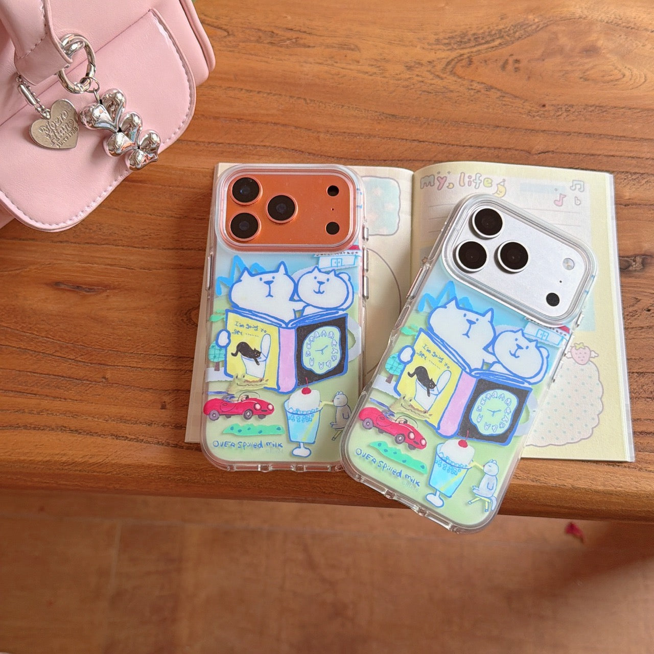 Top view of silver and bronze iPhones wearing cute cat doodle clear cases placed on an open diary.