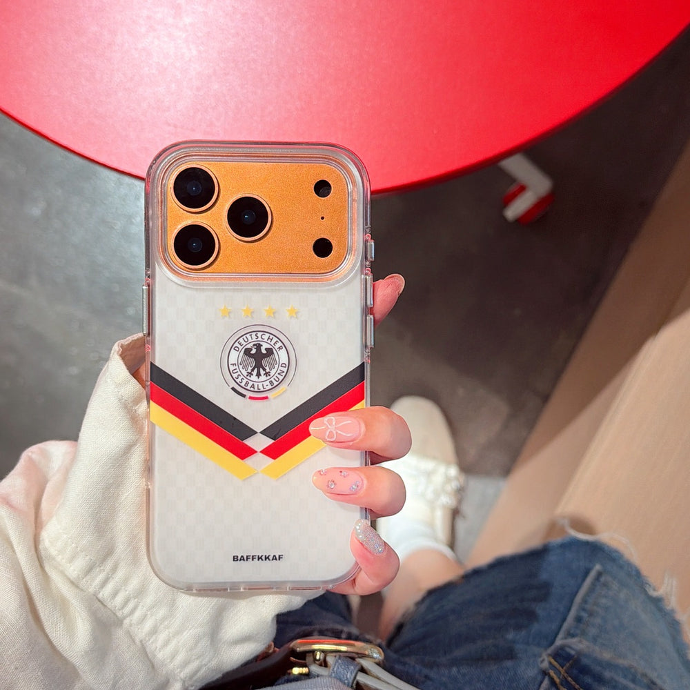 Top-down view of a hand holding the gold version of Germany soccer mirror phone case over a red floor.