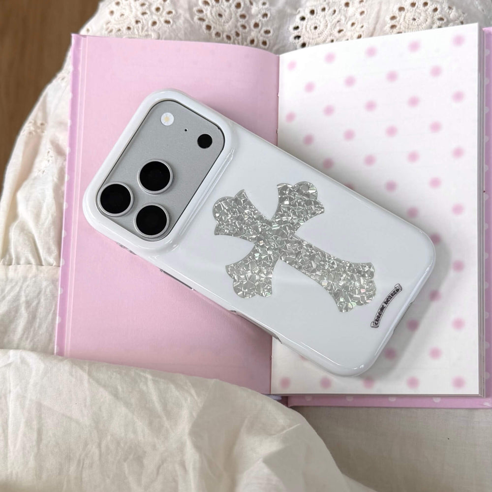 A gothic punk white phone case with a textured silver cross lying on a pink polka dot notebook.