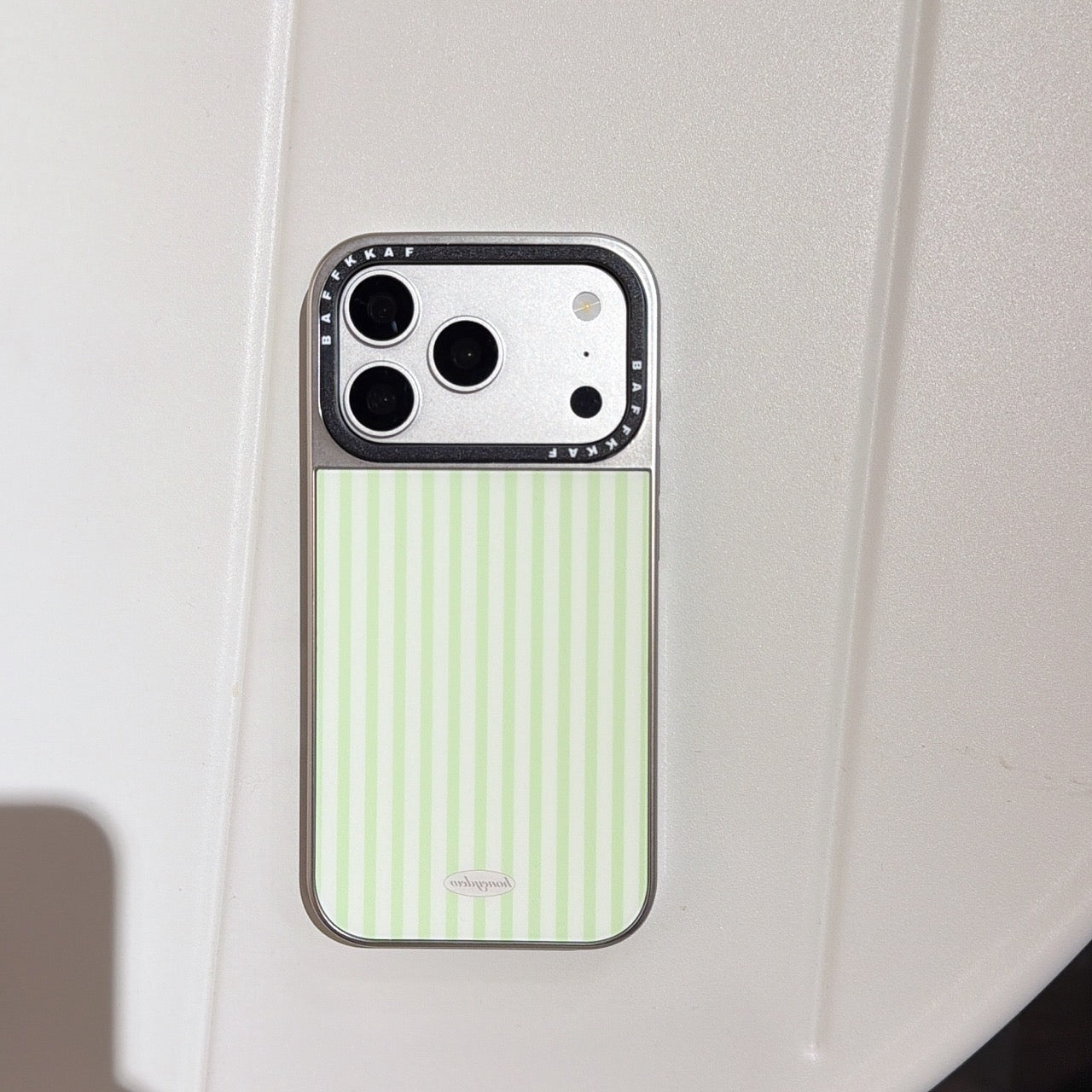 Studio product view of the green striped iPhone case with a silver camera protector on a white background.