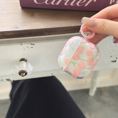 A close-up of a hand holding a pink cherry AirPods cover by its matching round carabiner clip.