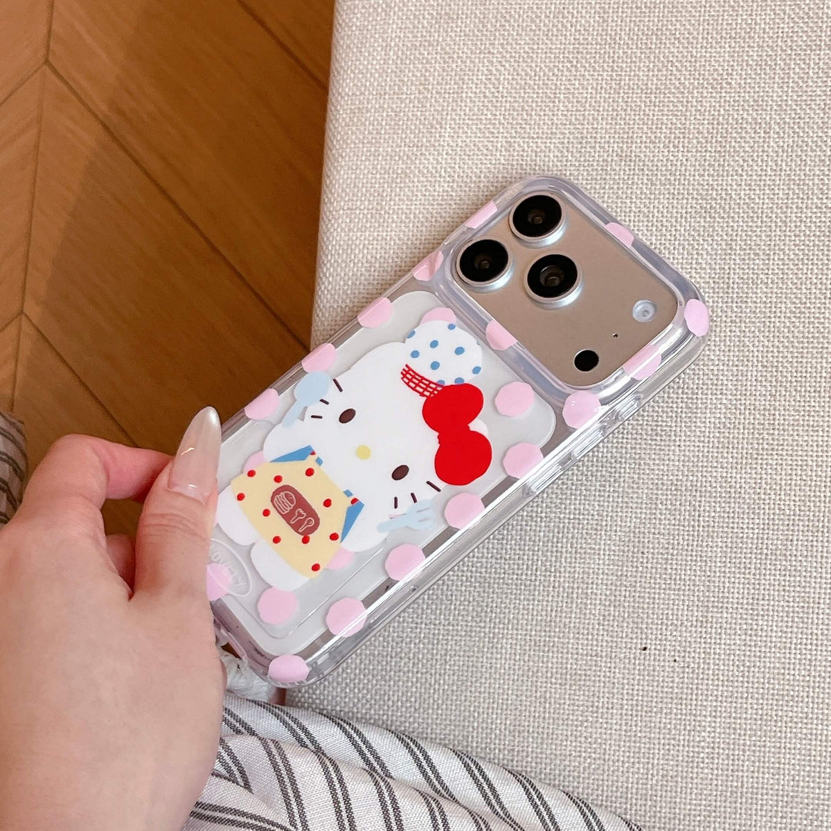 Close-up of a hand holding a clear pink polka dot phone case featuring a cute cartoon kitty wearing an apron.