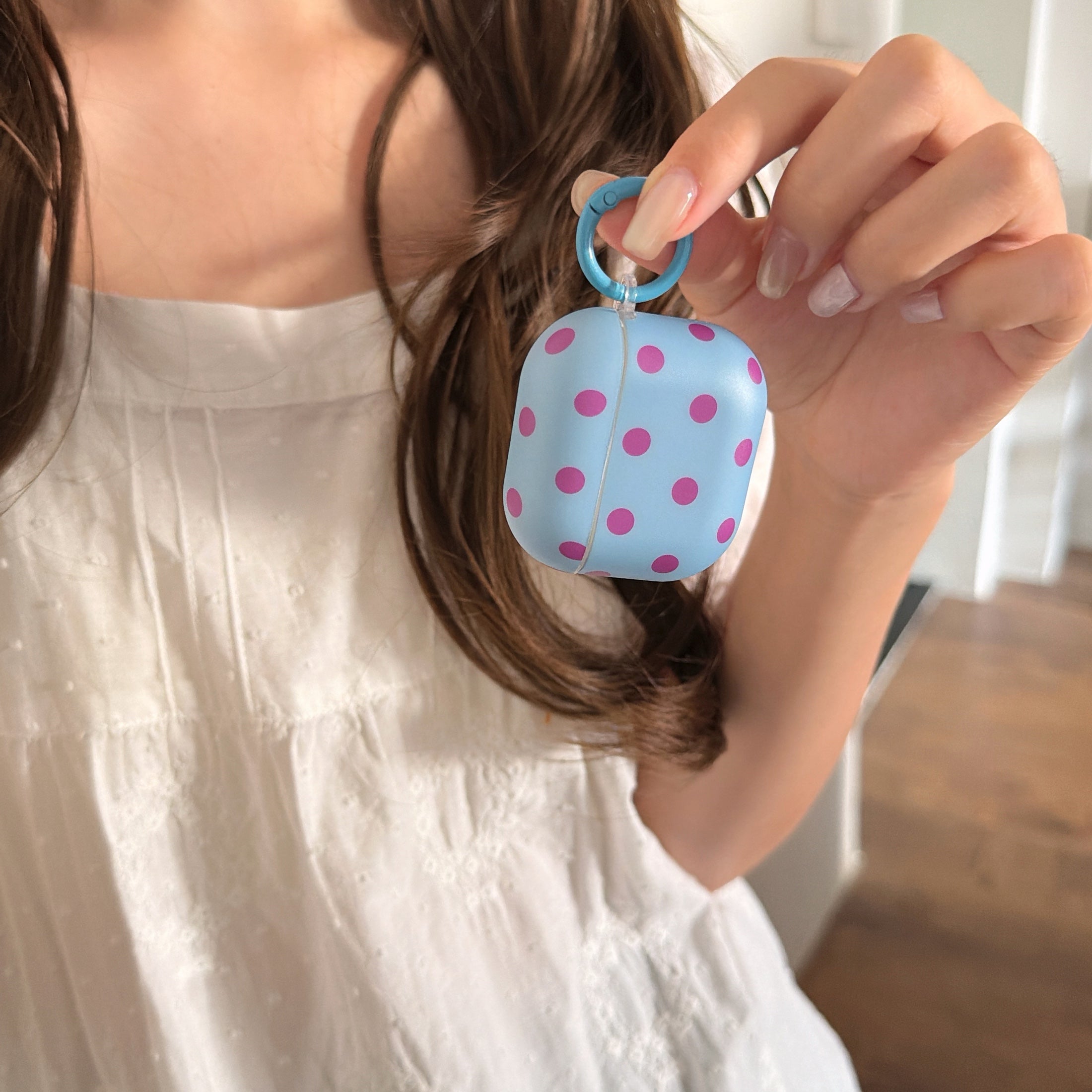 A hand lifting a cute light blue polka dot AirPods case up by its matching blue carabiner ring.