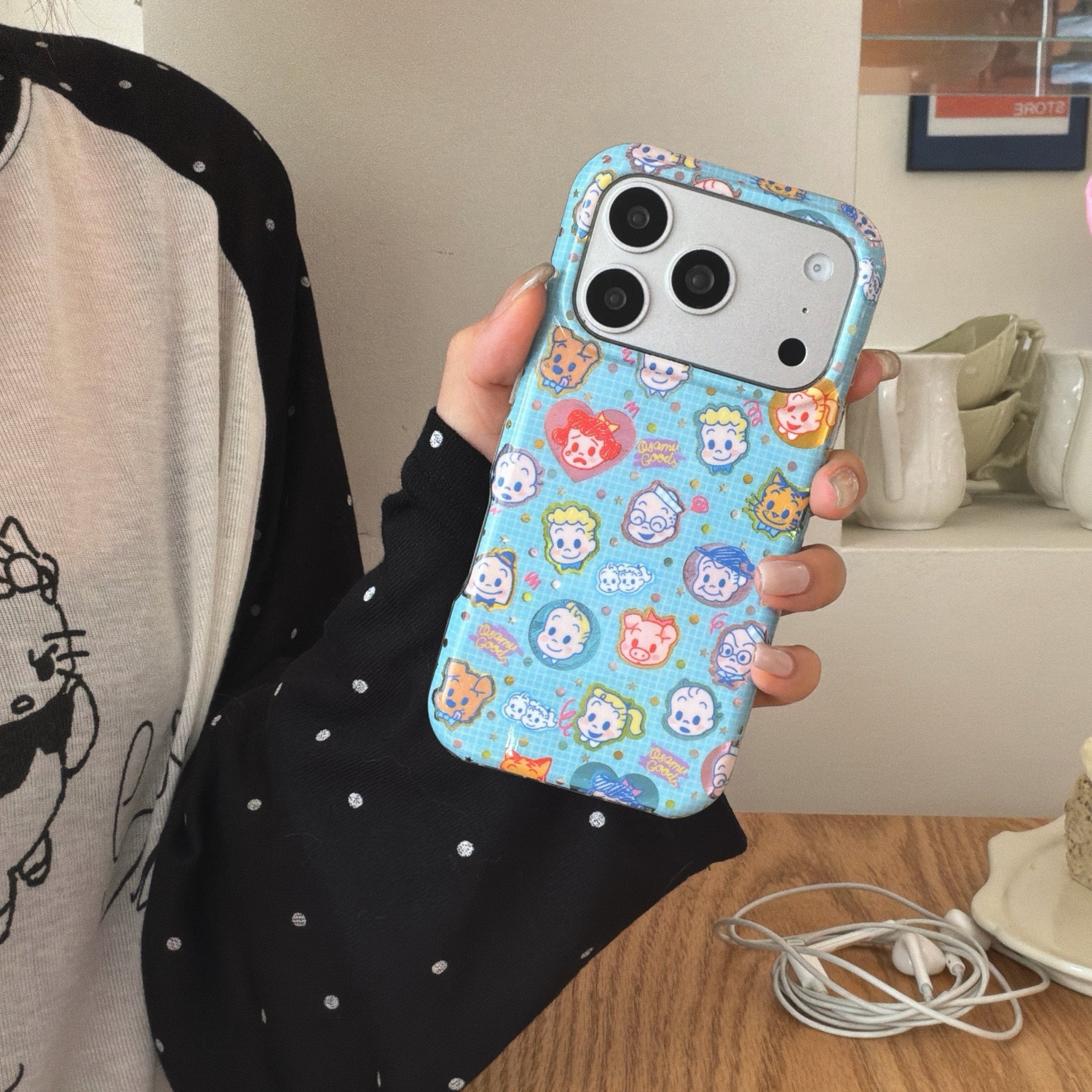 A close-up shot of a holographic glitter Osamu Goods case held above a wooden table with white earphones.