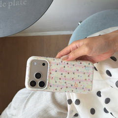 A hand holding a holographic glitter star phone case horizontally over a white polka dot outfit.